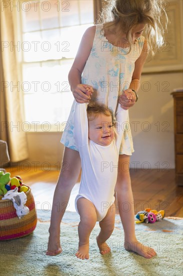 Caucasian girl helping baby walk