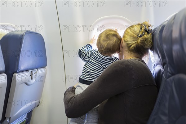 Caucasian mother and baby looking out airplane window