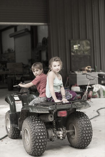 Caucasian children playing on four wheeler