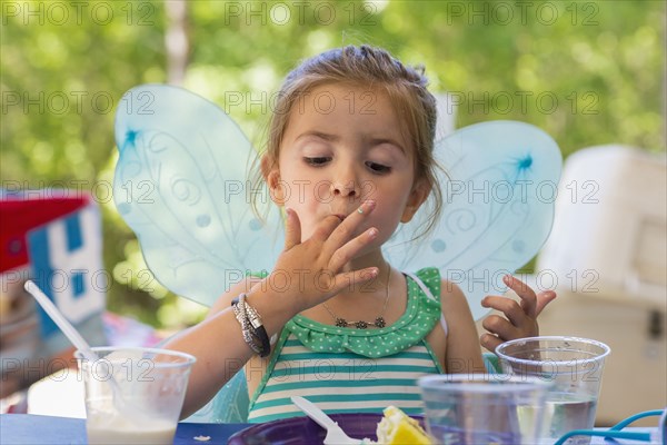 Caucasian girl eating cake at birthday party