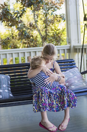 Caucasian girl holding brother on porch swing