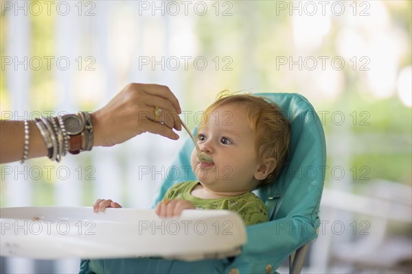 Caucasian mother feeding baby in high chair