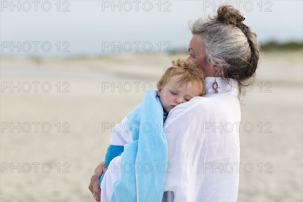 Caucasian woman carrying grandson on beach