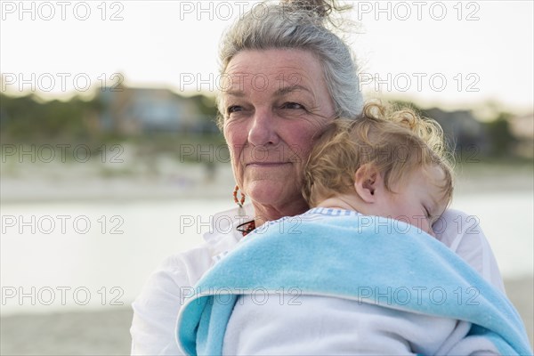 Caucasian woman carrying grandson on beach