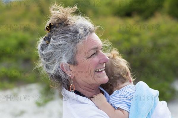 Caucasian woman carrying grandson on beach