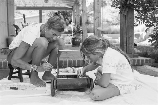 Caucasian mother and daughter painting toy on porch