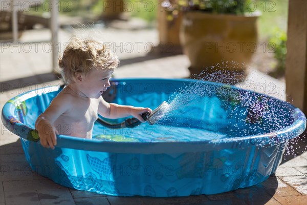 Caucasian baby playing with hose in wading pool