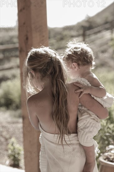 Caucasian girl carrying baby brother on porch