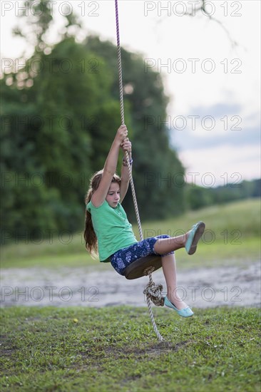 Caucasian girl playing on rope swing