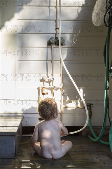 Nude Caucasian toddler playing with hose