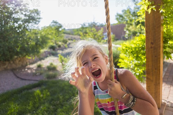 Caucasian girl playing on rope swing