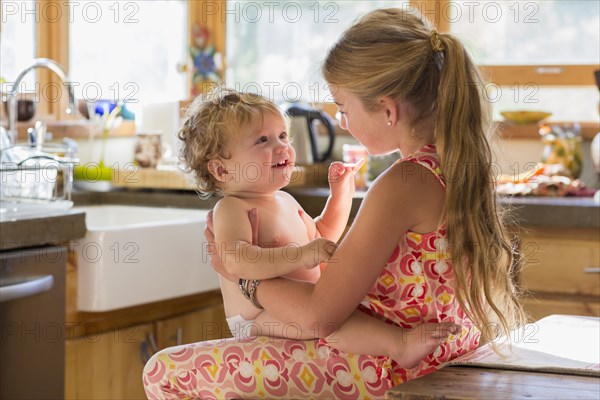 Caucasian girl holding toddler brother in kitchen