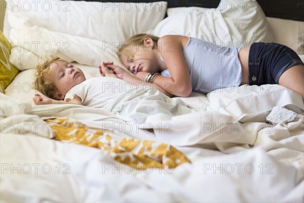 Caucasian girl and toddler brother asleep on bed