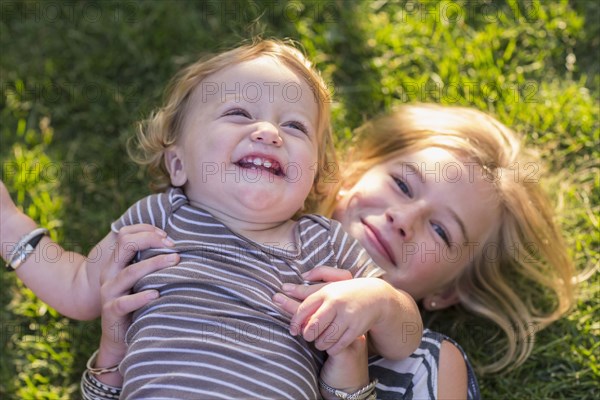 Caucasian sister holding baby brother in grass