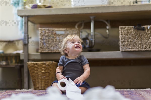 Caucasian baby unraveling toilet paper in bathroom