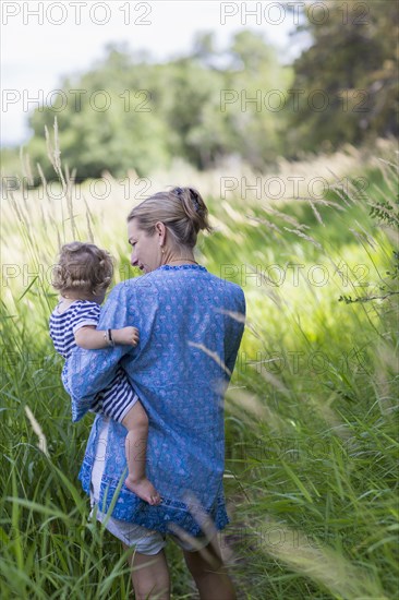 Caucasian mother carrying baby son in grassy field