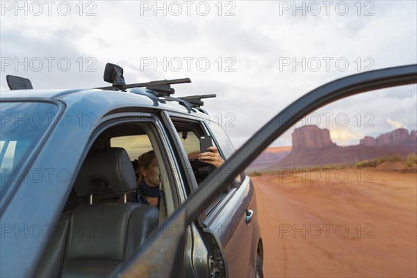 Caucasian girl taking cell phone photograph from car