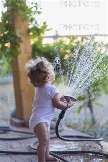 Caucasian baby boy playing with hose on patio