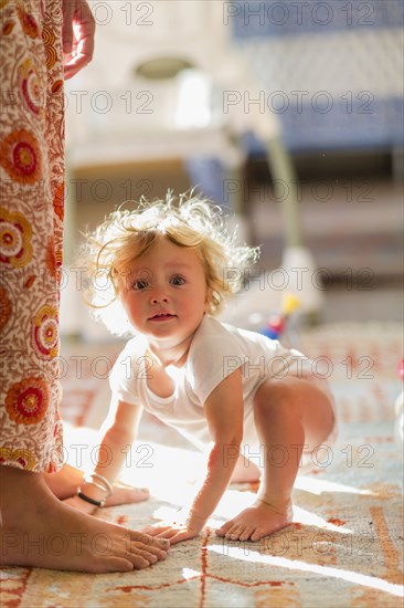 Caucasian baby boy crouching by feet of mother