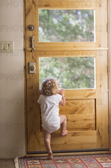 Caucasian baby boy peering out door window