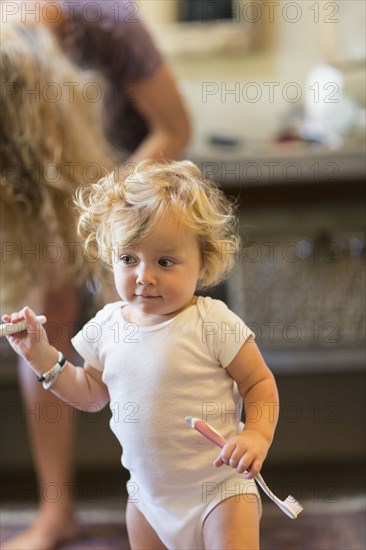 Caucasian baby boy holding toothbrush in bathroom