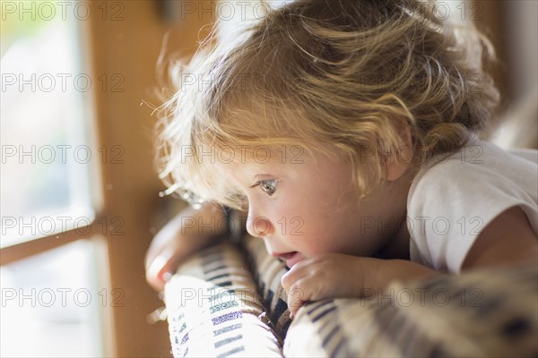 Caucasian baby boy peering over back of sofa in living room