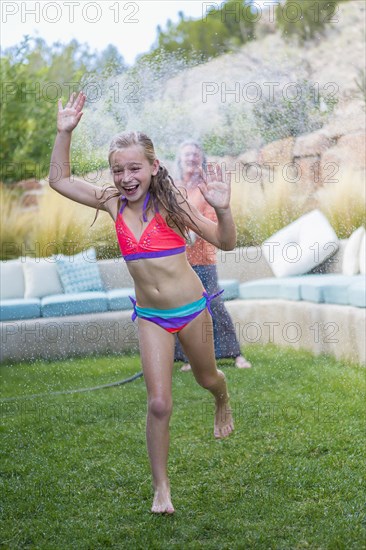 Caucasian grandmother spraying granddaughter with water in backyard