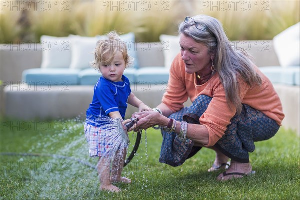 Caucasian grandmother and baby grandson watering lawn with hose