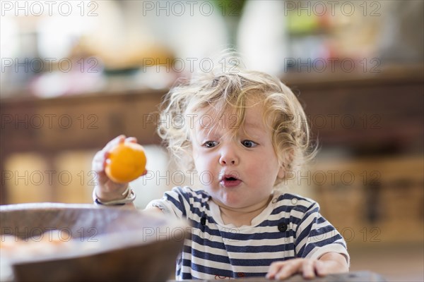 Surprised Caucasian baby boy examining fruit