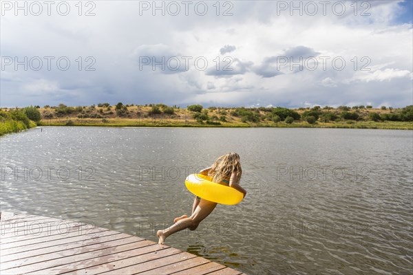 Mixed race teenage girl in inflatable ring jumping into still lake