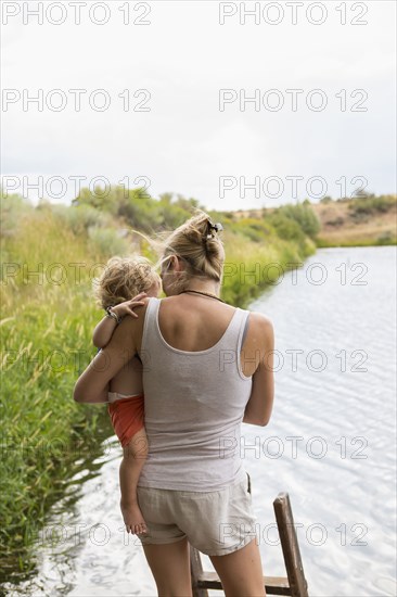 Caucasian mother holding baby son near lake