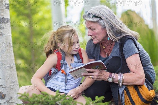 Caucasian grandmother and granddaughter reading guidebook while hiking