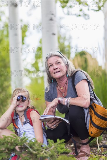 Caucasian grandmother and granddaughter using binoculars while hiking