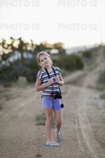 Caucasian girl carrying camera on rural dirt road