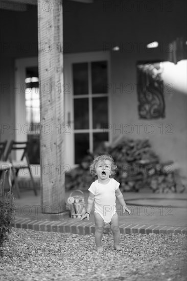 Caucasian baby boy standing on gravel in backyard