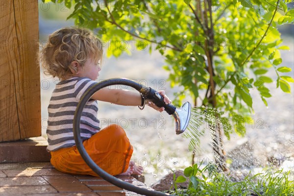 Caucasian baby boy watering plants from back patio