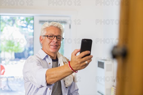 Older Hispanic artist taking cell phone photograph of art in studio