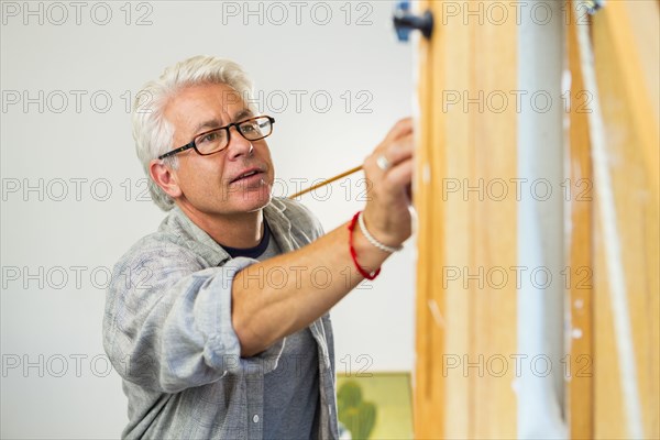 Older Hispanic artist painting in studio