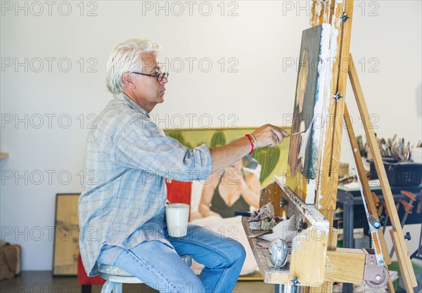 Older Hispanic artist painting in studio