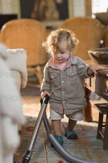 Caucasian baby boy vacuuming living room rug