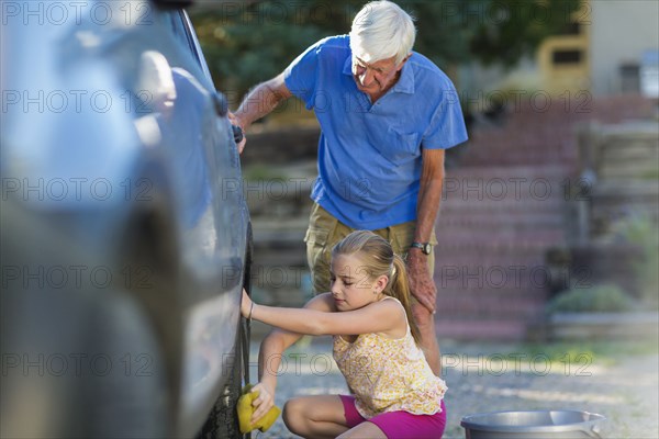 Caucasian grandfather and granddaughter washing car outdoors