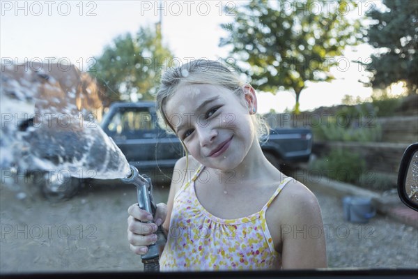 Caucasian girl spraying water from hose outdoors