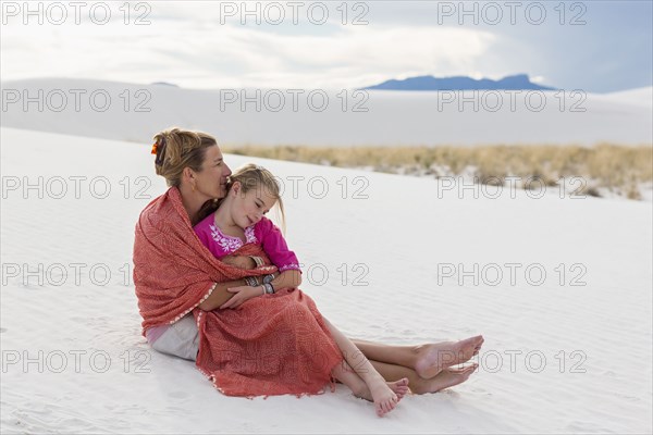 Caucasian mother and daughter wrapped in blanket on sand dune