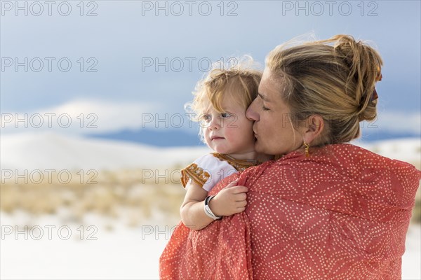 Caucasian mother and son wrapped in blanket on sand dune