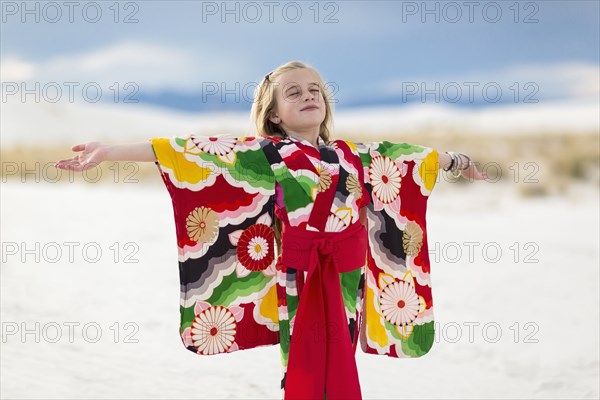Caucasian girl standing with arms outstretched on sand dune