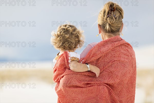 Caucasian mother and son wrapped in blanket on sand dune