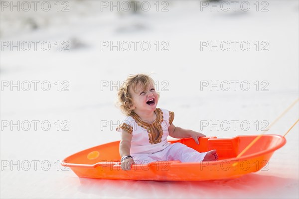 Caucasian boy sitting in sled on sand dune