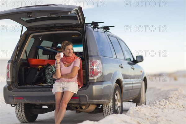 Caucasian woman leaning on car drinking coffee