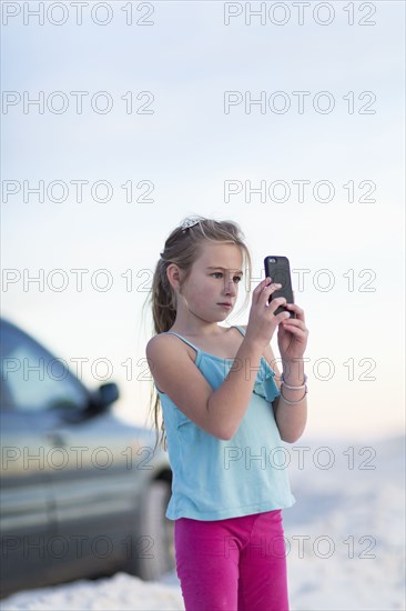 Caucasian girl taking cell phone photograph near car