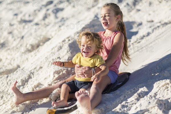 Caucasian brother and sister sledding on sand dune